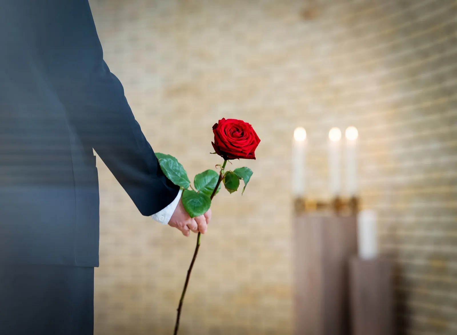 Hand mit einer roten Rose in der Trauerhalle