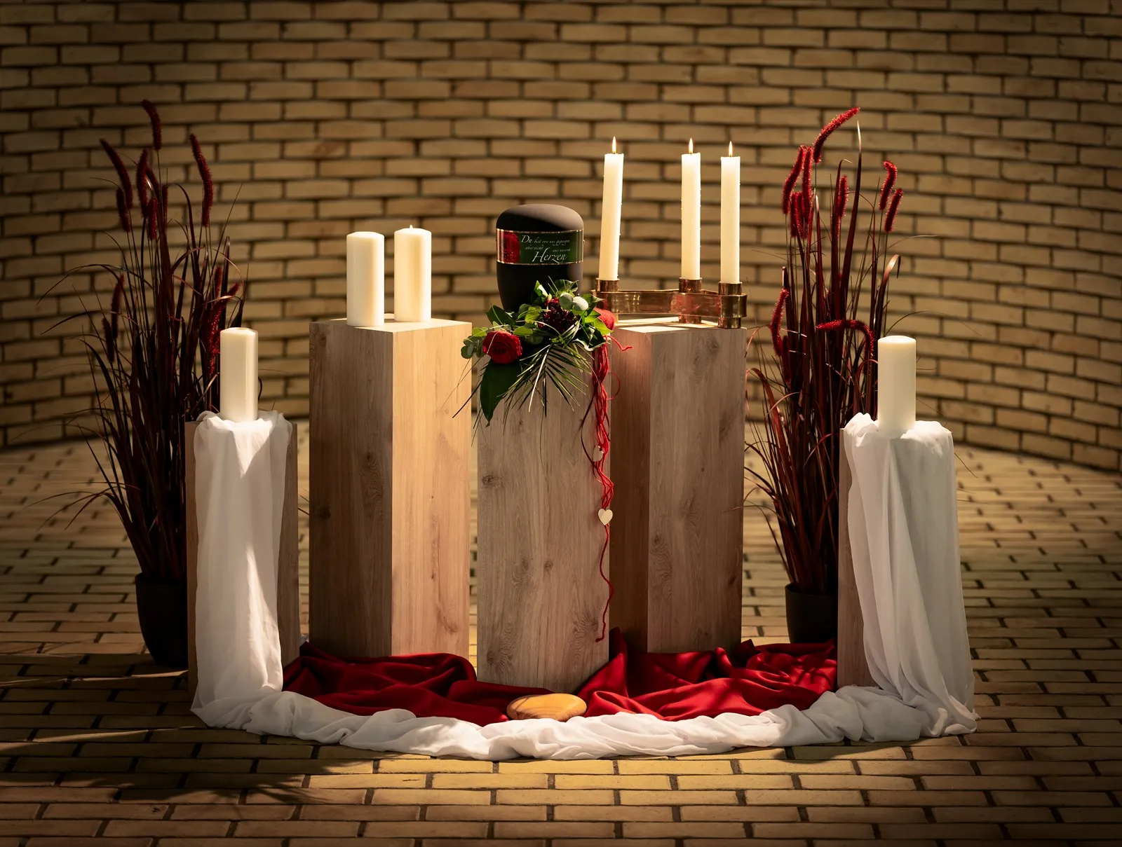 Trauerhalle mit Kerzen, Holzstelen und rotem Blumenschmuck